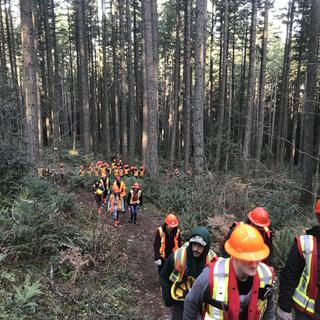 Students wearing safety gear hiking up a forest path.
